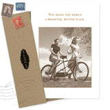 A sepia-toned "A Better Place Thank You Card" by Shannon Martin Design shows two women with a tandem bike and reads, "You make the world a brighter, better place." Includes matching envelope with vintage stamps. Made in USA.