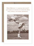 The March To The Beat Birthday Card by Shannon Martin Design showcases a vintage majorette woman with baton and feathered hat, kicking her leg below a cheerful birthday message—printed on recycled paper.