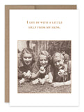 Three women relax on the grass, each cradling baby chicks, under the caption: "I get by with a little help from my hens." This sepia-toned image captures a timeless vintage aesthetic, much like a classic photograph. Available as the "Help From Hens Friendship Card" by Shannon Martin Design.