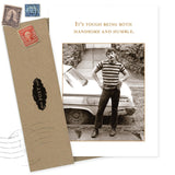 The Handsome Birthday Card by Shannon Martin Design features a photo of a man in stripes and jeans by a car with the message, "It’s tough being both handsome and humble." Includes an envelope with vintage-style stamps. Made in USA.