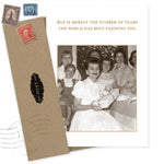 The Enjoying You Birthday Card by Shannon Martin Design features a sepia photo of a smiling woman with children holding a gift. Made in the USA from recycled paper, it reads: Age is merely the number of years the world has been enjoying you.