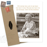 The Shannon Martin Design Never Too Late Birthday Card features a vintage photo of an elderly woman in glasses and a crocheted shawl holding a plate, with the message: It’s never too late to be what you want—unless you want to be younger!.