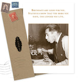 A sepia photo of a man blowing out birthday candles is featured on the Shannon Martin Design "Longer You Live Birthday Card." Next to it, vintage greeting cards and an envelope with vintage stamps complete this celebratory set.