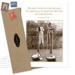 The Don't Stop Playing Birthday Card by Shannon Martin Design features a sepia photo of two people on stilts, smiling in a garden. Printed on recycled paper in the USA, it comes with an envelope.