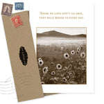 The Walk Beside Us Sympathy Card by Shannon Martin Design features sepia sunflowers, a mountain backdrop, and the quote: "Those we love don’t go away, they walk beside us every day." Includes brown envelope with vintage stamps. Made in USA.