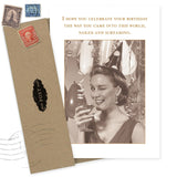 The Into This World Birthday Card by Shannon Martin Design features a sepia-toned vintage image of a woman in a party hat, winking with a drink amid balloons, and the cheeky message: "Celebrate your birthday like you came into this world—naked and screaming.