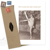 The "It's A Good Day Birthday Card" by Shannon Martin Design features a sepia photo of a woman high kicking by a picket fence, paired with a brown recycled envelope. The card reads, "IT'S A GOOD DAY FOR A GOOD DAY!"—ideal for vintage photo lovers.