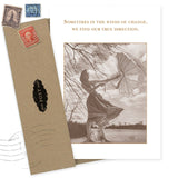 The Winds Encouragement Card by Shannon Martin Design features a sepia-toned vintage photo of a woman with an umbrella and the quote, "Sometimes in the winds of change, we find our true direction." Includes a vintage-style envelope and old postage stamps. Made in the USA.