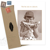 The Melon Thank You Card by Shannon Martin Design features a sepia photo of a child in a cap eating watermelon with "You're one in a melon" above. Made in the USA, it includes a brown envelope with vintage stamps and a postal seal.