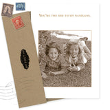 The Shannon Martin Design Shenanigans Birthday Card, made in the USA, displays a sepia photo of two smiling girls and the message "You’re the she to my nanigans." A brown envelope with vintage postage stamps is beside it.
