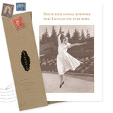 The Glad Born Birthday Card by Shannon Martin Design features a vintage-style woman leaping in a dress with the message, “This is your annual reminder that I’m glad you were born.” Includes a recycled brown envelope with old stamp designs.