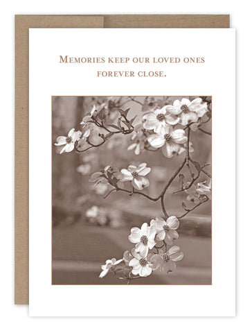 The Memories Sympathy Card by Shannon Martin Design features sepia-toned dogwood flowers with the phrase Memories keep our loved ones forever close. Made in the USA from recycled paper, its mounted on a brown background for a vintage feel.