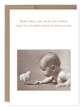 A sepia-toned vintage photo of a baby lying on their stomach, facing a small chick. The Shannon Martin Design card reads, Room In Your Heart Baby Card: Sometimes, the smallest things take up the most room in your heart.