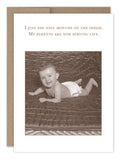 A sepia-toned card features a smiling baby in a diaper on a quilt, with the text: I just did nine months on the inside. My parents are now serving life. The Nine Months Baby Card by Shannon Martin Design is paired with a kraft envelope.