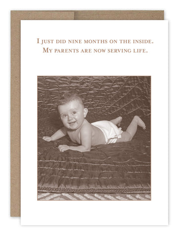 A sepia-toned photo of a smiling baby on a quilt, captioned humorously with I just did nine months on the inside. My parents are now serving life, is featured on the Nine Months New Baby Card by Shannon Martin Design. Made in the USA.