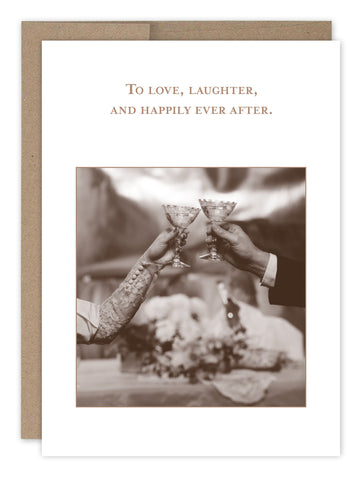 The Happily Ever After Wedding Card by Shannon Martin Design features a sepia photo of two hands toasting with champagne on recycled paper. The card reads, To love, laughter, and happily ever after, with a bouquet backdrop, celebrating moments made in the USA.