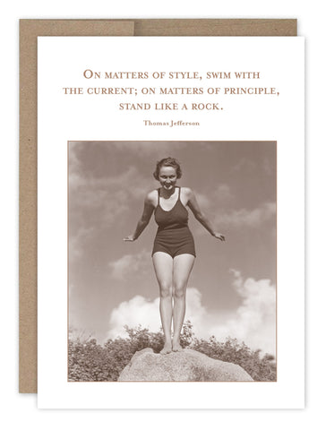 The Stand Like A Rock Encouragement Card by Shannon Martin Design features a vintage image of a woman in a swimsuit on a rock with the quote: On matters of style, swim with the current; on matters of principle, stand like a rock. It includes a brown envelope and is printed on FSC-certified recycled paper.