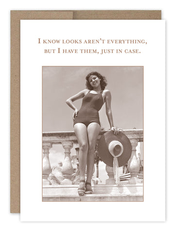 The Looks Arent Everything Birthday Card by Shannon Martin Design is a vintage-style card on recycled paper featuring a woman in a swimsuit with a sun hat, leaning on a stone railing. It reads, I know looks aren’t everything, but I have them, just in case, and comes with a Kraft envelope.