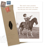 The "You Don't Stop Laughing Birthday Card" by Shannon Martin Design features a sepia cowboy playing guitar on horseback, alongside the quote: "You don’t stop laughing because you grow old; you grow old because you stop laughing," plus a vintage-style envelope.