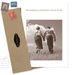 The Together Anniversary Card by Shannon Martin Design features a sepia photo of a couple holding hands in a field beneath the words "Together is a beautiful place to be," paired with a recycled brown envelope and vintage stamps.