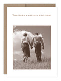 The Together Anniversary Card by Shannon Martin Design features a sepia photo of a couple holding hands in a grassy field under a blue sky, with the words: Together is a beautiful place to be. Made in the USA.
