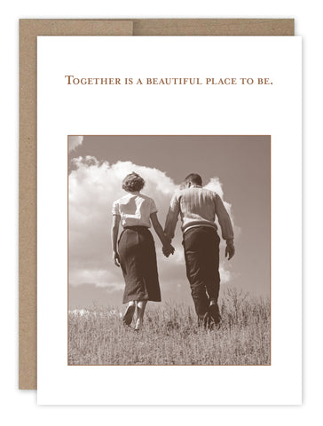 The Together Anniversary Card by Shannon Martin Design features a sepia photo of a couple holding hands in a grassy field under a blue sky, with the words: Together is a beautiful place to be. Made in the USA.
