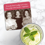 The Friends Don't Judge Coaster by Shannon Martin Design, featuring a vintage photo of three smiling women and the phrase "Friends don’t judge each other. They judge other people...together," sits beside a glass of lime and mint water.