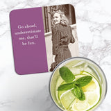 The Go Ahead Coaster by Shannon Martin Design features a vintage photo of a smiling, crowned woman with the phrase, "Go ahead, underestimate me, that’ll be fun," on a retro, cork-backed surface. A citrusy drink sits nearby on marble.