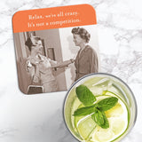 The We're All Crazy Coaster by Shannon Martin Design, a retro cork-backed coaster with a vintage photo and the quote “Relax, we’re all crazy. It’s not a competition,” is shown beside a refreshing citrus drink with mint and ice.