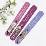Three Shannon Martin Design "Don't Look Emery Boards," featuring vintage photos of women and funny sayings, are arranged side by side on a white surface next to blooming white flowers and green leaves.