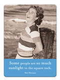A smiling woman in a striped shirt leans against a wooden post at the beach. Below her, the Sunlight Magnet by Shannon Martin Design shines—ideal for vintage photography fans or as a sturdy magnet to brighten your fridge.