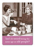 Two women in vintage outfits sip tea on a couch, smiling. A tray displays a tea set and the “Same Age Magnet” by Shannon Martin Design. Caption: “Isn’t it weird being the same age as old people?”.