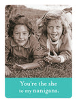 Two kids lie on grass, smiling at the camera. One playfully sticks out their tongue, looking as if they found a treasure in the fridge. Text reads, Youre the she to my nanigans. Product: Shenanigans Magnet by Shannon Martin Design.