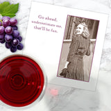 The Go Ahead Me Napkin by Shannon Martin Design features a vintage photo of a smiling woman in a dress and hat with the text "Go ahead, underestimate me, that'll be fun," perfect for parties with drinks and grapes on marble.