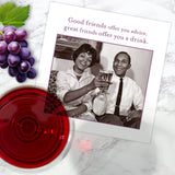 The Offer You Advice Napkin by Shannon Martin Design is displayed on a marble surface with grapes, red wine, and a card showing friends clinking glasses and the message: Good friends offer you advice, great friends offer you a drink.