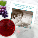 A Cake & Eat It, Too Napkin by Shannon Martin Design rests on a marble surface with grapes, red wine, and a card featuring a smiling woman and the text: I’d like to have my cake and eat it, and also yours.