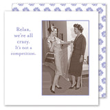 Two women in vintage clothing laugh together in a hallway. Beside them: "Relax, we’re all crazy. It’s not a competition." The Shannon Martin Design "We're All Crazy Napkin" features a blue floral border—ideal for your next gathering.