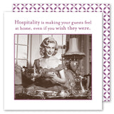A vintage-style photo of a smiling woman pours tea amid elegant sets and Shannon Martin Design Hospitality Napkins. Above, the text reads: "Hospitality is making your guests feel at home, even if you wish they were." Purple and white patterned border.