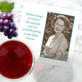 A glass of red wine and grapes sit beside a card and Shannon Martin Design’s Better Left Unsaid Napkin, which features a black-and-white photo of a smiling woman and the text: Some things are better left unsaid, but I’m probably going to say them anyway.