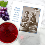A black-and-white birthday card from Shannon Martin Design features two women in hats on a log, with grapes, red wine, and the Hats Off Napkin nearby. Text: Happy birthday to the friend everyone wishes they had.