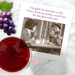 The Glad We Met Napkin by Shannon Martin Design features a vintage photo of two women laughing at a cafe with the text: "I’m glad we met later in life. I don’t think my mother would have let me play with you." Party napkins, grapes, and red wine nearby.