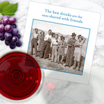 A vintage photo of friends with drinks is shown next to a glass of red wine, grapes, and Shannon Martin Design's "The Best Drinks Napkin" on marble. The napkin reads: The best drinks are the ones shared with friends.