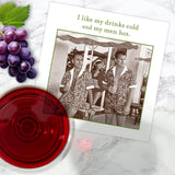 A glass of red wine and grapes sit beside a Shannon Martin Design “Drinks Cold, Men Hot” napkin featuring two men with drinks on a beach—ideal for fun parties with stylish, eco-friendly, biodegradable supplies.