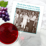 A vintage photo of cheerful friends with drinks is pictured beside a glass of red wine, grapes, and Shannon Martin Design’s Drink Happy Napkin, which reads: Drink what makes you happy with friends who make you laugh.