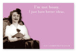A vintage-style photograph by Shannon Martin Design, showcasing a smiling woman sitting in an armchair and wearing a white blouse with a dark skirt. The pink background highlights the text, "I'm not bossy, I just have better ideas," reminiscent of humor stickies. Designed in 2011, this image features on the Not Bossy Sticky Note.