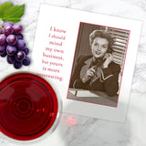 A Shannon Martin Design "My Own Business Napkin" on marble beside grapes, vintage napkins, and red wine. The card displays a vintage woman on the phone with the text: “I know I should mind my own business, but yours is more interesting.”.