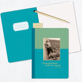 The Every Great Dream Journal by Shannon Martin Design, featuring a blue jewel-toned cover with a child’s photo and inspirational quote, rests on an open lined notebook, alongside a pencil and vintage tickets on a white surface.