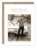A vintage photo featuring a man in a striped shirt and jeans confidently standing by a classic car on a cobblestone street graces the cover of the "Handsome Birthday Card" by Shannon Martin Design. The image, printed on recycled paper, includes the text: "It's tough being both handsome and humble.
