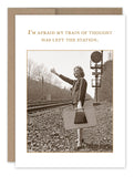 A sepia-toned image of a woman in vintage attire standing on a railway track decorates the "Train Of Thought Birthday Card" by Shannon Martin Design. Carrying a suitcase and waving, she's accompanied by the text: "I'm afraid my train of thought has left the station," set against a brown recycled paper background. This card is part of an award-winning collection.