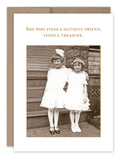 Two young girls in vintage dresses stand arm-in-arm, smiling in front of a house. Text above them reads, "She who finds a faithful friend, finds a treasure." The scene is reminiscent of vintage photos with a nostalgic, sepia-toned appearance, similar to the design on recycled paper by Shannon Martin Design's She Who Finds Birthday Card.